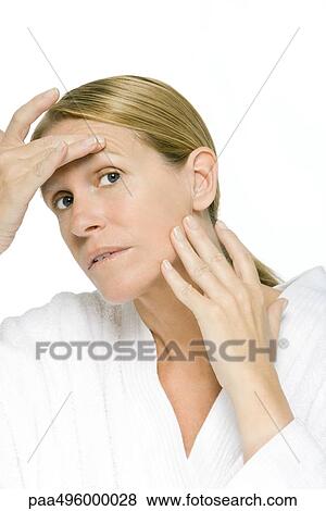 Stock Photo - Mature woman examining her face, close-up. Fotosearch