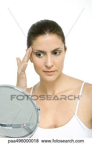 Woman looking at self in mirror, touching temple View Large Photo Image Stock Photo - Woman looking at self in mirror, touching temple. Fotosearch