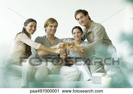 Stock Image - Adult friends clinking champagne glasses, smiling at camera. Fotosearch