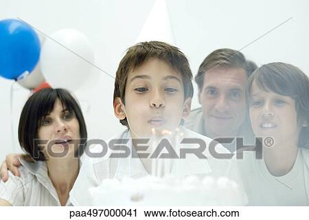 Boy blowing out candles on birthday cake, family watching View Large Photo Image Stock Image - Boy blowing out candles on birthday cake, family watching. Fotosearch