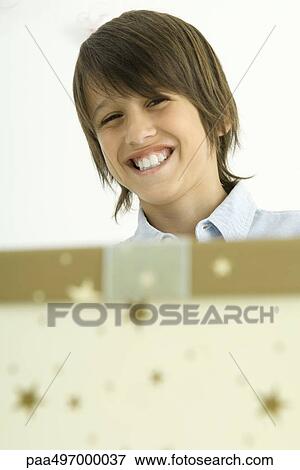 Boy looking over wrapped box, smiling at camera, focus on background View Large Photo Image Stock Photo - Boy looking over wrapped box, smiling at camera, focus on background. Fotosearch