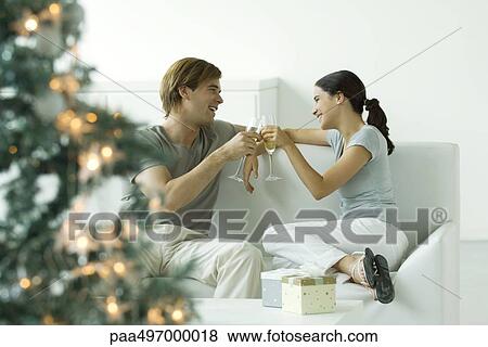 Couple making a toast with champagne, Christmas tree in foreground View Large Photo Image Stock Photo - Couple making a toast with champagne, Christmas tree in foreground. Fotosearch