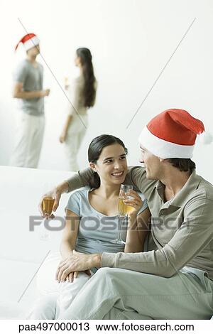 Couple sitting on sofa, drinking champagne, man wearing Santa hat View Large Photo Image Stock Image - Couple sitting on sofa, drinking champagne, man wearing Santa hat. Fotosearch