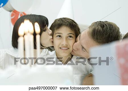 Stock Photo - Family behind birthday cake with lit candles, parents kissing boy on cheeks. Fotosearch