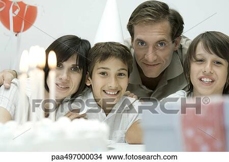 Family in front of birthday cake with lit candles, smiling at camera View Large Photo Image Picture - Family in front of birthday cake with lit candles, smiling at camera. Fotosearch