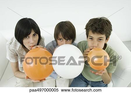 Stock Photography - Mother and two sons inflating balloons, woman and one son looking at camera. Fotosearch