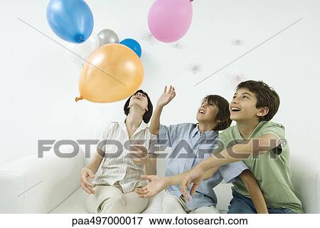 Stock Photo - Mother and two sons playing with balloons, looking up. Fotosearch