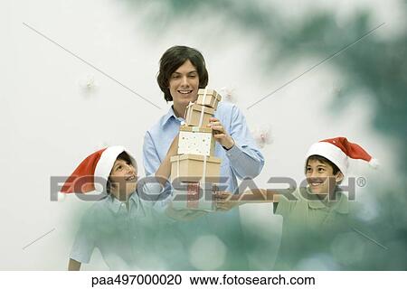 Stock Image - Three brothers stacking Christmas gifts, smiling, selective focus. Fotosearch