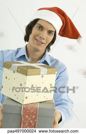 Young man holding Christmas gifts toward camera, smiling View Large Photo Image Picture - Young man holding Christmas gifts toward camera, smiling. Fotosearch