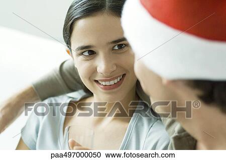 Young woman smiling at man in Santa hat, close-up View Large Photo Image Stock Image - Young woman smiling at man in Santa hat, close-up. Fotosearch