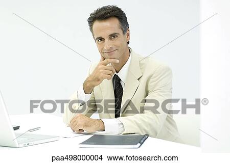 Picture - Business executive sitting at desk, smiling at camera, portrait. Fotosearch