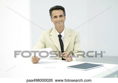Businessman sitting at desk, smiling at camera View Large Photo Image Stock Photograph - Businessman sitting at desk, smiling at camera. Fotosearch