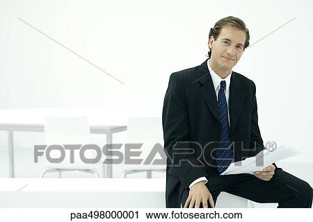 Stock Image - Executive holding document, smiling at camera. Fotosearch