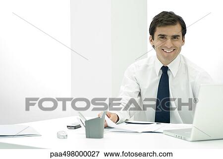 Male professional sitting at desk, smiling at camera View Large Photo Image Stock Photo - Male professional sitting at desk, smiling at camera. Fotosearch