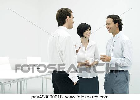 Professionals chatting, holding coffee cups, smiling View Large Photo Image Stock Photo - Professionals chatting, holding coffee cups, smiling. Fotosearch
