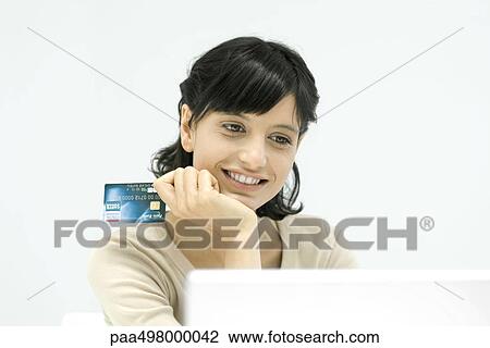 Woman holding credit card, looking at laptop computer, smiling View Large Photo Image Stock Image - Woman holding credit card, looking at laptop computer, smiling. Fotosearch