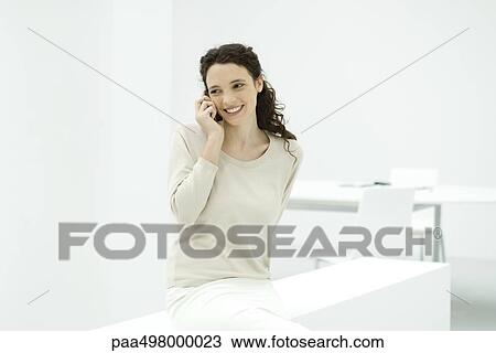 Stock Image - Woman in office, using cell phone, smiling. Fotosearch