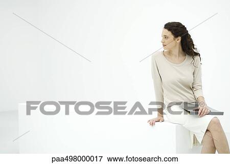 Young female professional sitting on ledge, holding binder, looking over shoulder View Large Photo Image Stock Photo - Young female professional sitting on ledge, holding binder, looking over shoulder. Fotosearch