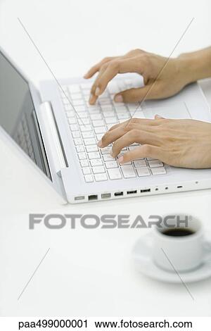 Stock Image - Hands typing on laptop computer, coffee cup in foreground. Fotosearch