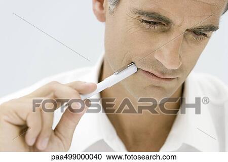 Man holding pen up to corner of mouth, looking down, close-up View Large Photo Image Stock Image - Man holding pen up to corner of mouth, looking down, close-up. Fotosearch