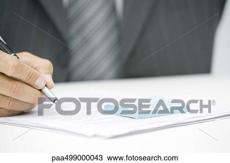 Stock Image - Man with adhesive note and document, holding pen, cropped view. Fotosearch
