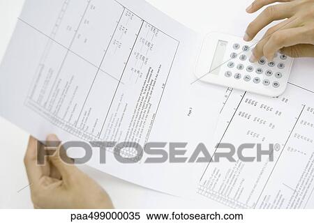 Stock Photography - Person holding document, using calculator, cropped view of hands. Fotosearch