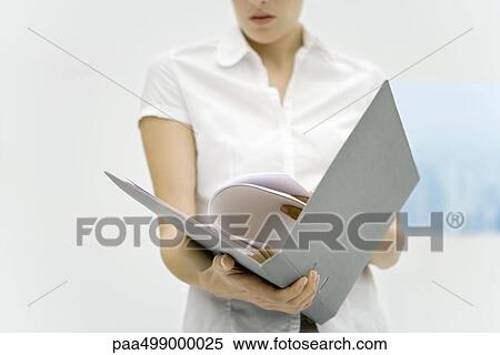 Stock Photography - Woman holding binder, reading document, cropped view. Fotosearch