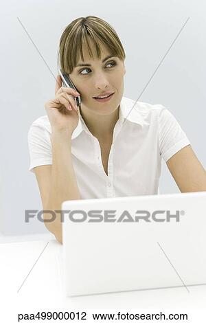 Woman sitting in front of laptop computer, using cell phone, looking away View Large Photo Image Stock Image - Woman sitting in front of laptop computer, using cell phone, looking away. Fotosearch