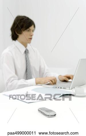 Young professional working at desk, focus on cell phone in foreground View Large Photo Image Stock Image - Young professional working at desk, focus on cell phone in foreground. Fotosearch