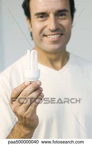 Man holding energy efficient light bulb, smiling at camera View Large Photo Image Stock Image - Man holding energy efficient light bulb, smiling at camera. Fotosearch