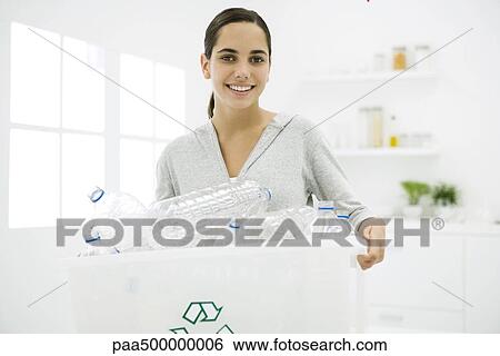Stock Photograph - Teen girl carrying recycling bin full of plastic bottles, smiling at camera. Fotosearch