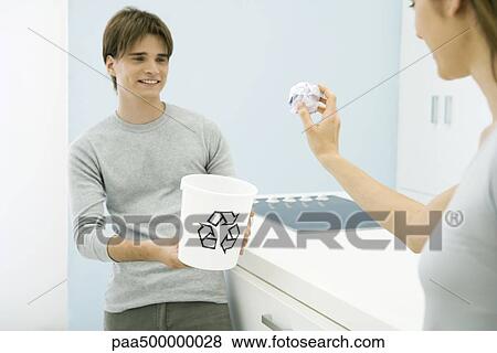 Stock Photo - Woman aiming paper ball at recycling bin in young man's hands, cropped view. Fotosearch