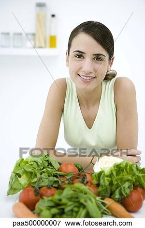 Stock Photo - Woman leaning behind assorted fresh vegetables, smiling at camera. Fotosearch