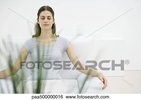 Stock Photograph - Woman sitting in armchair, eyes closed, plant in foreground. Fotosearch