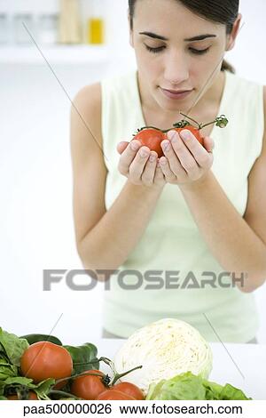 Stock Photograph - Woman smelling ripe vine tomatoes, close-up. Fotosearch