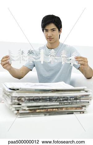 Young man with stacked newspapers, holding tree shapes cut out of paper, looking at camera View Large Photo Image Stock Image - Young man with stacked newspapers, holding tree shapes cut out of paper, looking at camera. Fotosearch