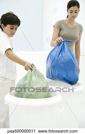 Stock Image - Young woman and boy placing garbage bags in separate garbage cans. Fotosearch
