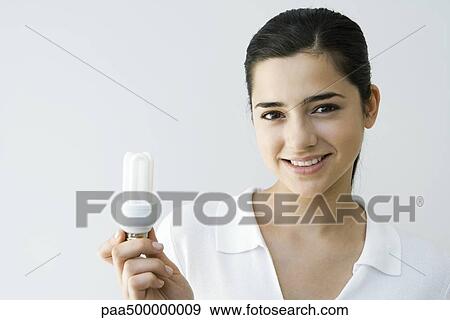 Young woman holding energy-saving light bulb, smiling at camera View Large Photo Image Stock Photo - Young woman holding energy-saving light bulb, smiling at camera. Fotosearch