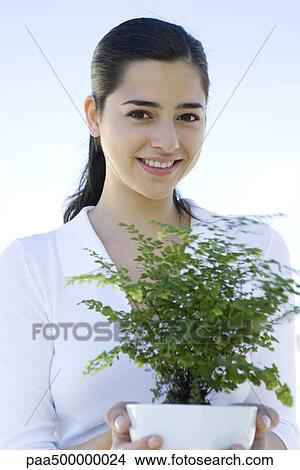 Young woman holding potted plant, smiling at camera View Large Photo Image Picture - Young woman holding potted plant, smiling at camera. Fotosearch