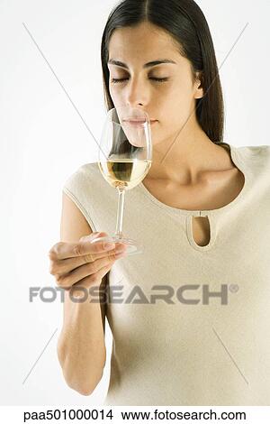 Picture - Woman smelling glass of white wine, eyes closed. Fotosearch