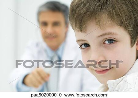 Boy smiling at camera, doctor holding stethoscope in the background View Large Photo Image Stock Image - Boy smiling at camera, doctor holding stethoscope in the background. Fotosearch