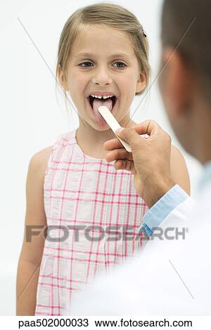 Stock Image - Doctor examining a girl's throat using a tongue depressor. Fotosearch