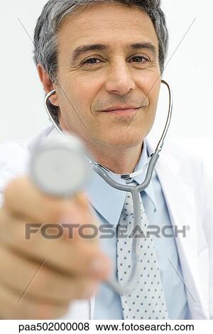 Doctor holding stethoscope toward camera, focus on background View Large Photo Image Stock Photo - Doctor holding stethoscope toward camera, focus on background. Fotosearch