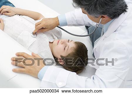 Doctor listening to young patient's heart, high angle view View Large Photo Image Picture - Doctor listening to young patient's heart, high angle view. Fotosearch