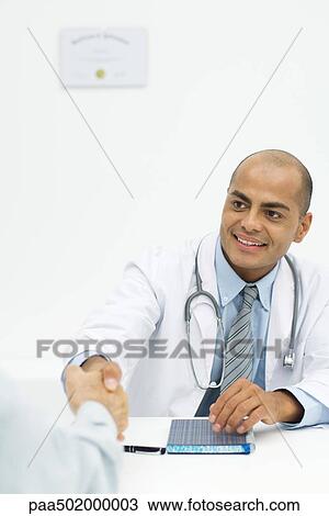 Stock Image - Doctor shaking hands with patient, over the shoulder view. Fotosearch