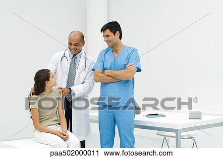 Stock Image - Doctor standing with hands on teen girl's shoulders, male nurse standing nearby. Fotosearch
