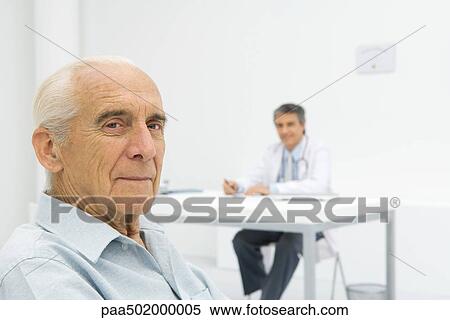 Doctor working at desk, focus on senior patient in foreground View Large Photo Image Stock Photography - Doctor working at desk, focus on senior patient in foreground. Fotosearch