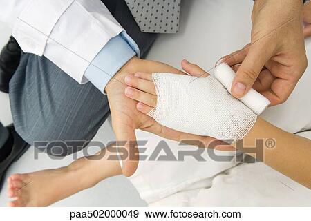 Stock Photo - Doctor wrapping a patient's hand in gauze, high angle view. Fotosearch