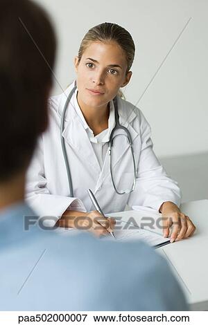 Stock Photo - Doctor writing at desk, patient in foreground. Fotosearch