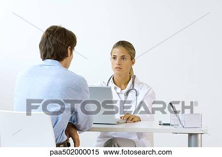 Female doctor sitting across from male patient at desk, using laptop computer View Large Photo Image Stock Photography - Female doctor sitting across from male patient at desk, using laptop computer. Fotosearch